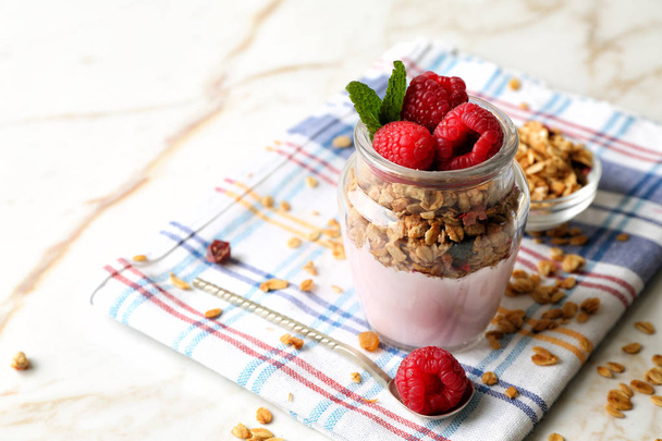 Glass jar of tasty yogurt with raspberry and oatmeal on table - Foto, afbeelding