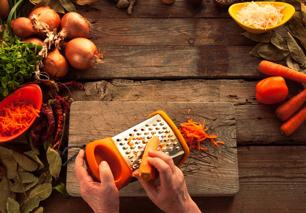 As mãos de mulher esfregam cenouras em um ralador
 - Foto, Imagem