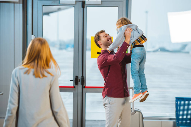 enfoque selectivo de padre feliz celebración en brazos hija cerca de la esposa en el aeropuerto
  - Foto, Imagen
