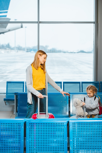 houkutteleva äiti seisoo söpö tytär tilalla nallekarhu lähellä matkatavaroita lentokentällä
  - Valokuva, kuva