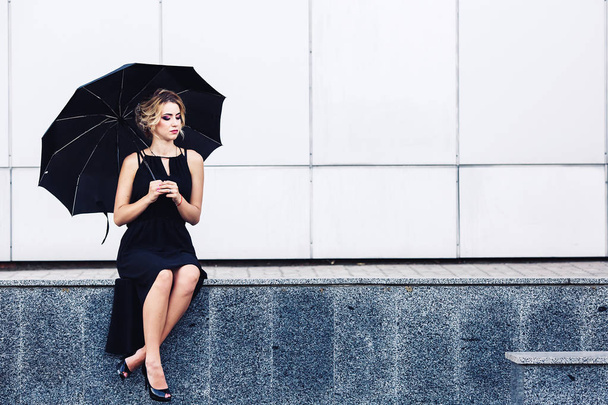 gorgeous woman with an umbrella sits on the parapet and waits. - Photo, Image