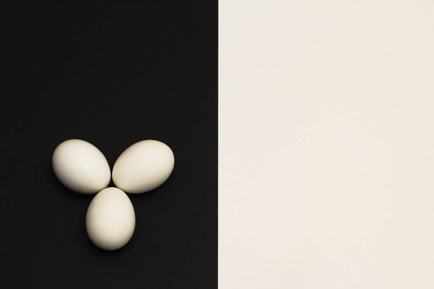 White chicken eggs on black part of contrasting black and white background. Minimalism style. - Foto, Imagen
