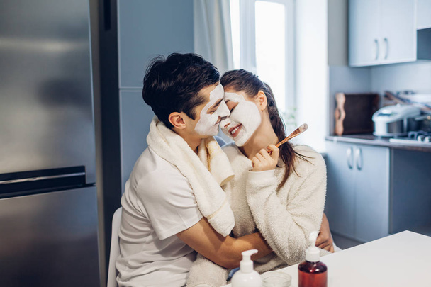 Joven pareja cariñosa abrazándose con máscaras faciales aplicadas en casa. Tratamiento de la piel. Gente feliz celebrando el día de San Valentín
 - Foto, Imagen