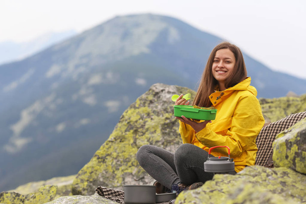 Young woman in yellow jacket have a picnic on top of the mountain.  - Photo, image