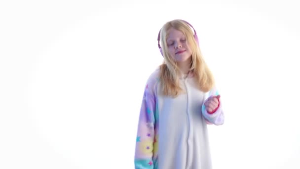 moderní móda - krásná blond dívka poslouchá hudbu se sluchátky a tančí na bílém pozadí v kigurumi pyžama - izolované na bílém - Záběry, video