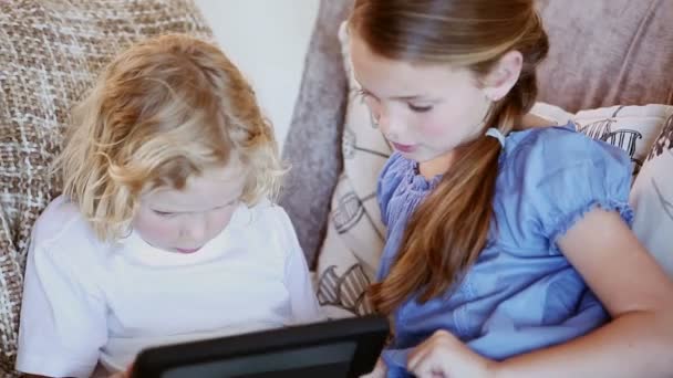 Siblings sitting on the couch while using a tablet computer - Πλάνα, βίντεο