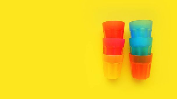 Plastic glass of various color isolated on yellow background - Φωτογραφία, εικόνα