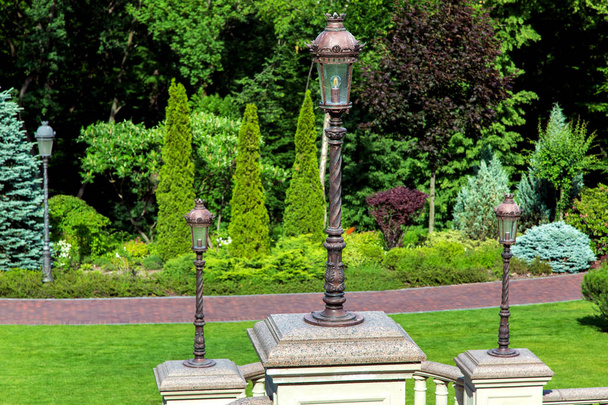 Vintage iron lantern on a marble pedestal in a park recreation area with a pedestrian walkway with landscape design and plantings. - Фото, изображение