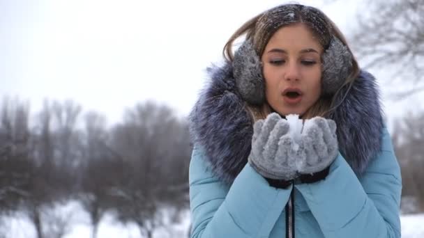 piękna młoda kobieta trzyma śnieg w dłoniach i wieje na nim - Materiał filmowy, wideo