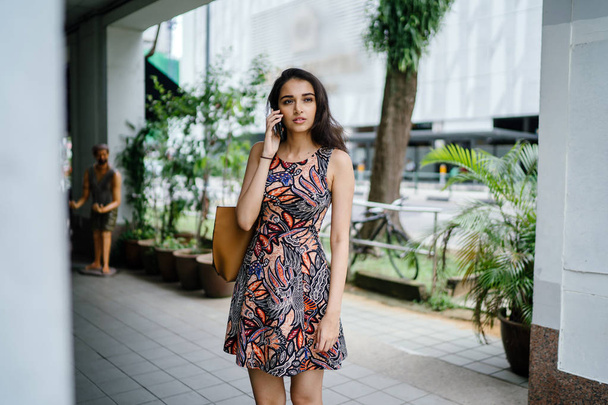 Young Indian Asian woman standing and talking on her smartphone on an urban street in a city in Asia during the day - 写真・画像
