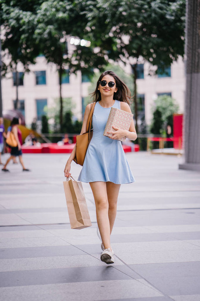 young, fashionable and happy young Indian Asian woman in a blue dress walking down a street in the shopping district  - Foto, Imagen