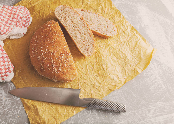 Свежеиспечённая буханка хлеба из цельнозерновой муки с отрубями на бумаге. Порезанный ножом
 - Фото, изображение