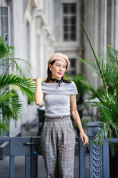 Portrait of a fashionable, elegant and beautiful middle-aged asian woman in the day. She is smiling as she poses in the grey corridor of a court house. - Foto, Imagen