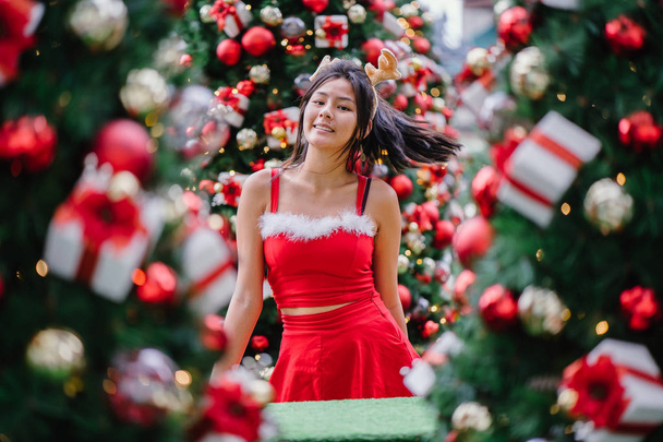 Portrait of a young Asian Chinese girl in a red Santarina costume dress. She is cute, pretty and attractive and is also wearing a reindeer headband  - Valokuva, kuva