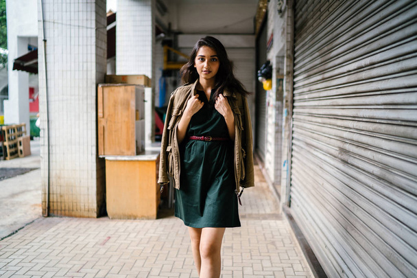 young, tall, slim and elegant Indian Asian woman poses for a portrait. She is wearing comfortable and stylish casual clothing and has a man's jacket draped over her shoulders.  - Фото, зображення