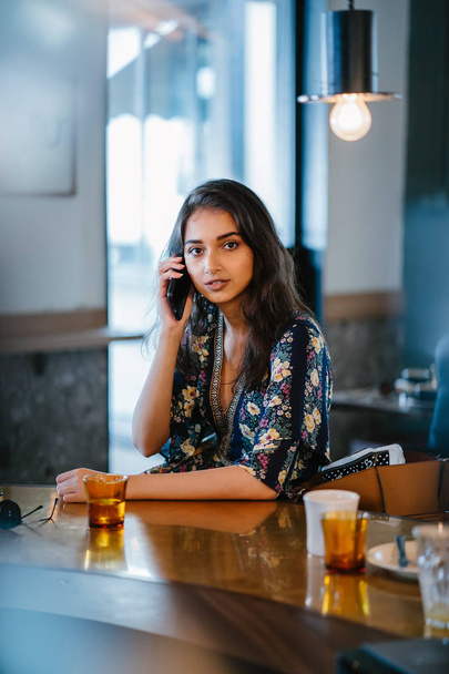Portrait of a young and attractive Indian Asian woman frowning as she talks on her smartphone in a cafe during the day - 写真・画像