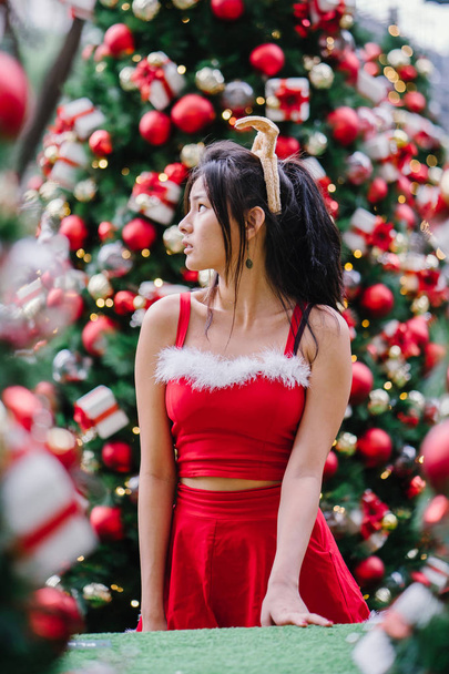 Portrait of a young Asian Chinese girl in a red Santarina costume dress. She is cute, pretty and attractive and is also wearing a reindeer headband  - Foto, Bild