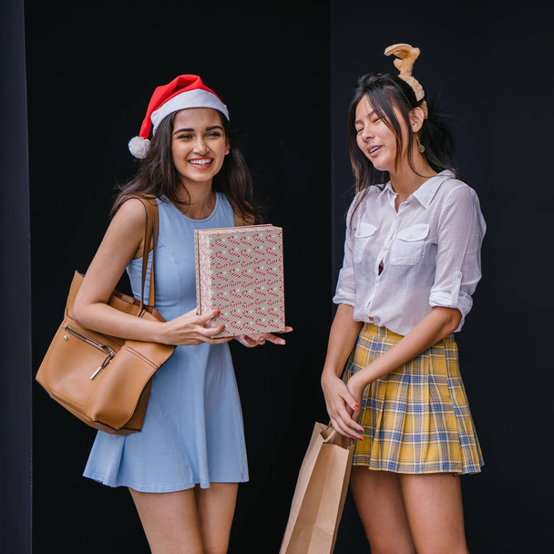 Two close friends exchange Christmas presents with one another on the holiday season. They are both Asian, one is Indian, the other Chinese. They are smiling happily as they exchange gifts. - Foto, imagen