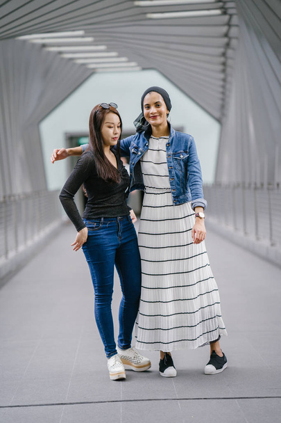 Two friends of different ethnicity on a bridge during the day. One is a Malay Muslim woman and the other is Chinese Asian. They are both young, energetic and attractive. - Fotó, kép