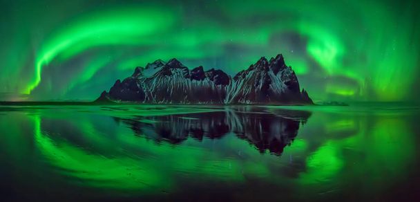 Reflections of aurora borealis around Vestrahorn mountains on Stokksnes black beach, Iceland  - Photo, Image