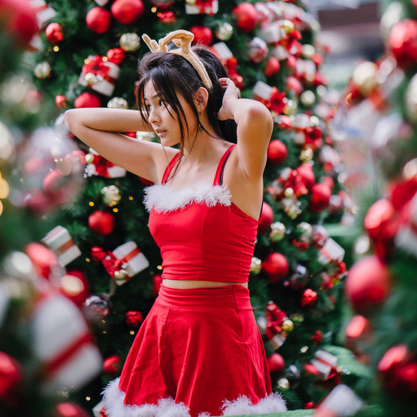 Portrait of a young Asian Chinese girl in a red Santarina costume dress. She is cute, pretty and attractive and is also wearing a reindeer headband  - Photo, image