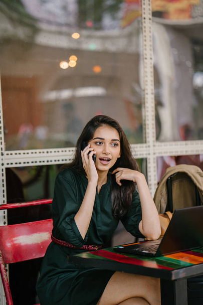 young Singpaorean Indian woman checking her smartphone as she takes a break from studying or working on her laptop during the day in a cafe - Фото, зображення