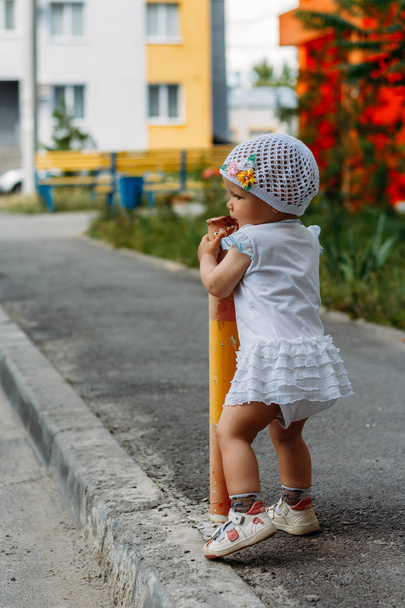 Urocza dziewczyna zabawy na letnie dni. dziewczynka stoi na ścieżce Przejście i trzyma do ogrodzenia, rur - Zdjęcie, obraz