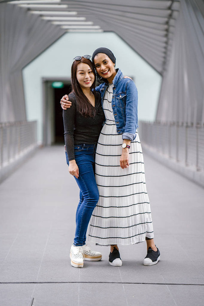 Two friends of different ethnicity on a bridge during the day. One is a Malay Muslim woman and the other is Chinese Asian. They are both young, energetic and attractive. - Φωτογραφία, εικόνα