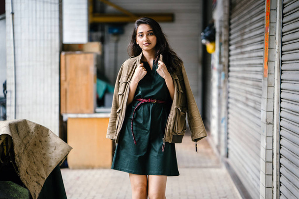 young, tall, slim and elegant Indian Asian woman poses for a portrait. She is wearing comfortable and stylish casual clothing and has a man's jacket draped over her shoulders.  - Фото, зображення