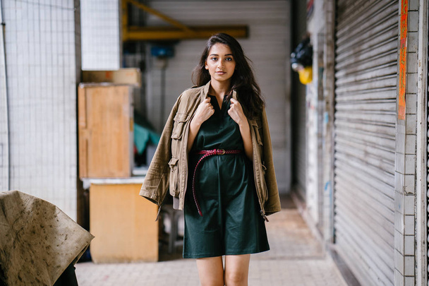 young, tall, slim and elegant Indian Asian woman poses for a portrait. She is wearing comfortable and stylish casual clothing and has a man's jacket draped over her shoulders.  - Foto, Imagen