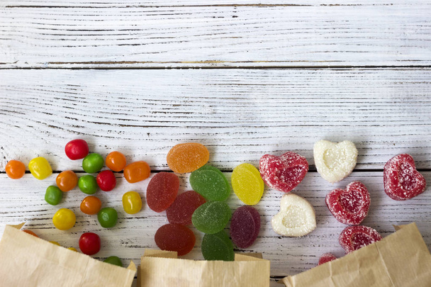 runde farbige Bonbons und Marmelade in einer Papiertüte auf einem Holztisch, helle Süßigkeiten, weißer Hintergrund - Foto, Bild