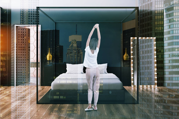 Woman in interior of bedroom with black and gray walls, wooden floor, gray master bed with vertical mirror near it and open bathroom door. Toned image double exposure - Foto, immagini