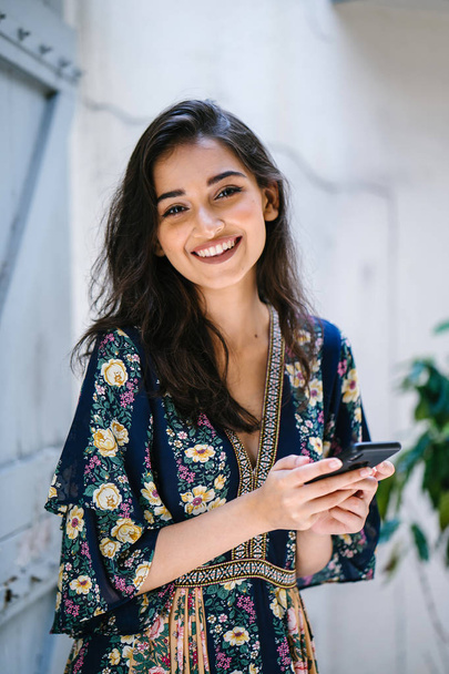 Portrait of a young, attractive and beautiful Indian Asian woman wearing a dress and sunglasses with her smartphone - Foto, imagen