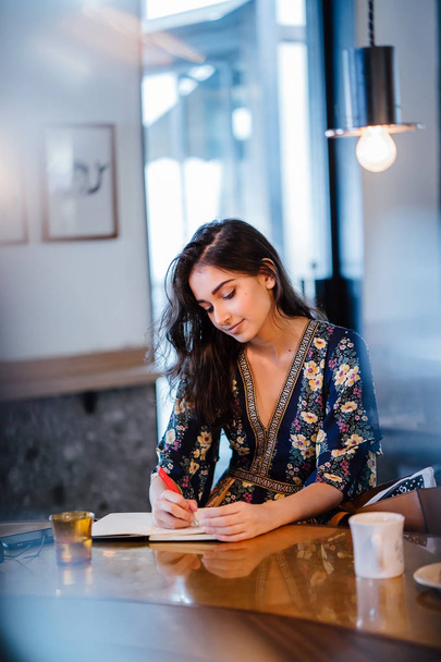 young Indian Asian woman sits at a cafe and is writing on her notebook with her pen - Фото, зображення