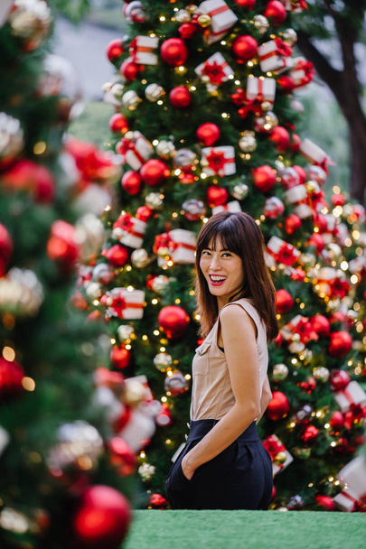 Chinese Asian tourist woman smiles and poses for a portrait with beautifully decorated Christmas trees during the day in the city - Valokuva, kuva