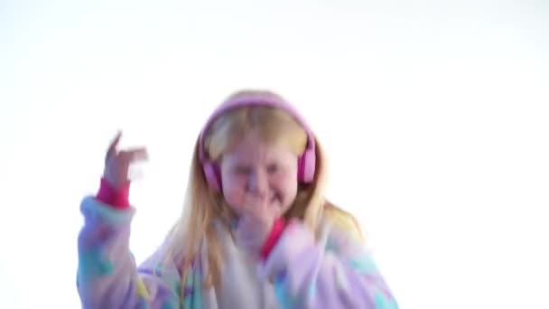 nowoczesnej mody - Piękna Blondynka dziewczyna słucha muzyki z słuchawki i taniec na białym tle w piżamie kigurumi - na białym tle - Materiał filmowy, wideo