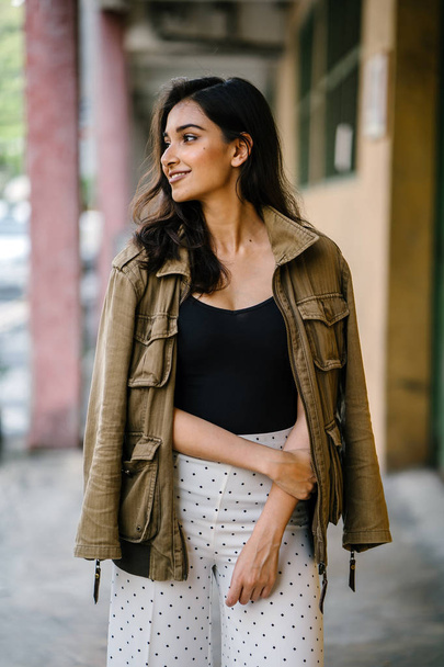 Portrait of a tall, beautiful, slim and elegant Indian Asian woman walking down a walkway in a city in Asia during the day. She is elegantly dressed and has a jacket draped over her shoulders. - Foto, afbeelding