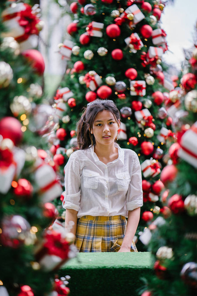 Chinese Asian tourist woman smiles and poses for a portrait with beautifully decorated Christmas trees during the day in the city. - Valokuva, kuva