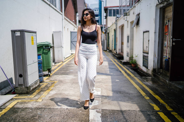 young, tall, slim and elegant Indian Asian woman in a casual outfit walks down an alley in a street in Asia during the day - Photo, Image