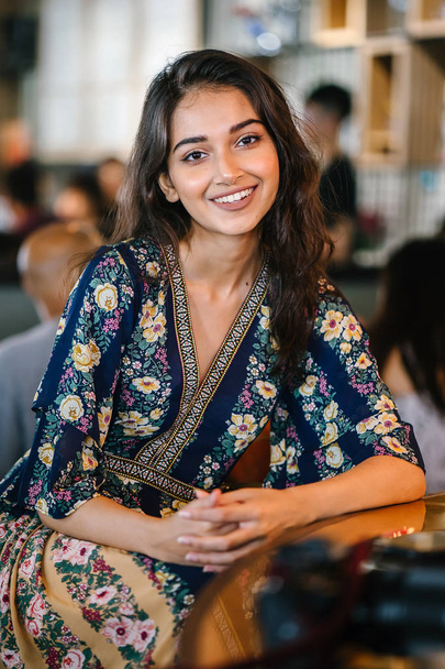 portrait head shot of a young, confident, and attractive Indian Asian girl in a warmly lit trendy cafe - Valokuva, kuva