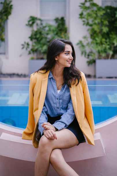 Fashionable, elegant and young Indian Asian woman in a retro outfit. She is wearing a yellow jacket draped over a comfortable summer outfit. - Photo, Image