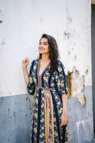 portrait of a tall, young, elegant and beautiful Indian Asian woman in flowing dress against a weathered wall on a street  - 写真・画像