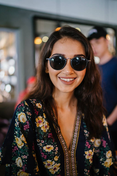 lifestyle close up portrait of a young, beautiful and gorgeous Indian Asian girl in sunglasses and a floral dress sitting in a cafe during the day - Φωτογραφία, εικόνα