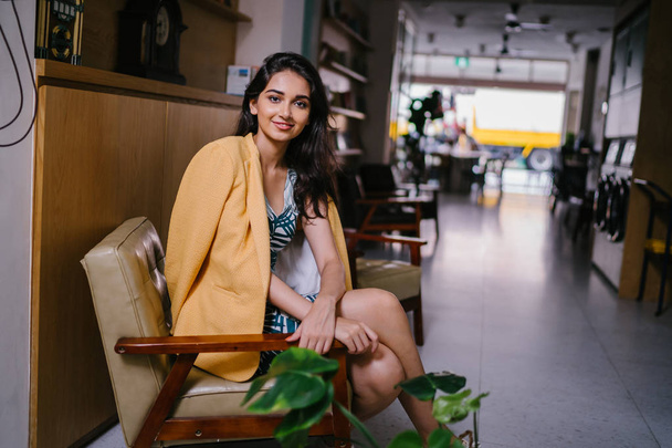 Fashionable, elegant and young Indian Asian woman in a retro outfit. She is wearing a yellow jacket draped over a comfortable summer outfit. - 写真・画像