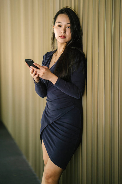 Portrait of a young and beautiful Asian Chinese woman holding smartphone - Foto, afbeelding