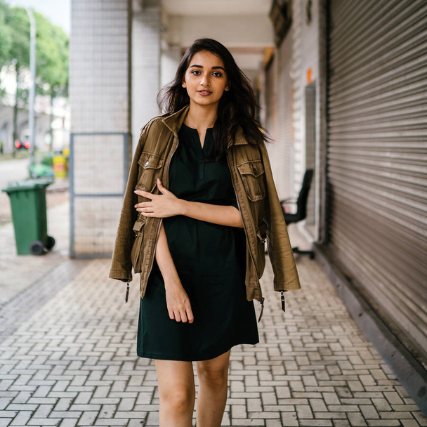 young, tall, slim and elegant Indian Asian woman poses for a portrait. She is wearing comfortable and stylish casual clothing and has a man's jacket draped over her shoulders.  - Foto, immagini