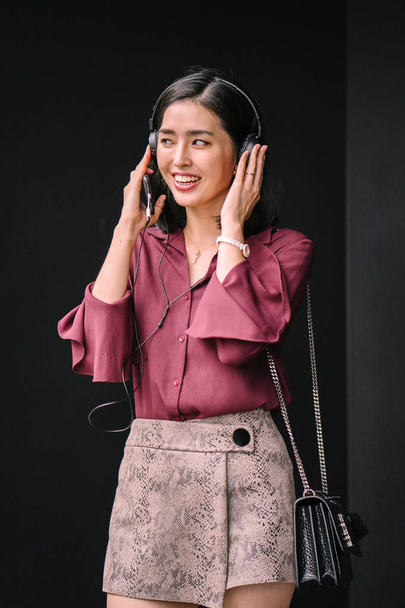 Portrait of a young Korean Asian woman smiling happily as she listens to music on her headphones - Фото, изображение