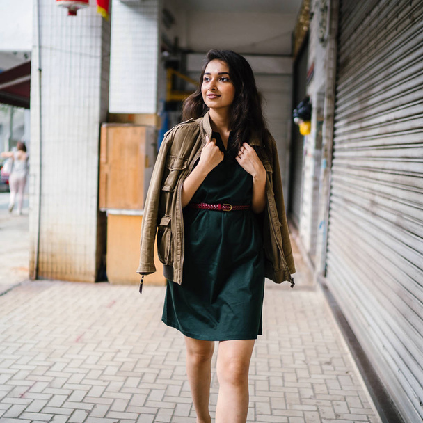 young, tall, slim and elegant Indian Asian woman poses for a portrait. She is wearing comfortable and stylish casual clothing and has a man's jacket draped over her shoulders.  - Fotoğraf, Görsel