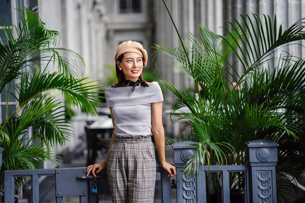 Portrait of a fashionable, elegant and beautiful middle-aged asian woman in the day. She is smiling as she poses in the grey corridor of a court house. - 写真・画像