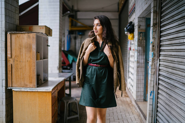 young, tall, slim and elegant Indian Asian woman poses for a portrait. She is wearing comfortable and stylish casual clothing and has a man's jacket draped over her shoulders.  - Photo, image